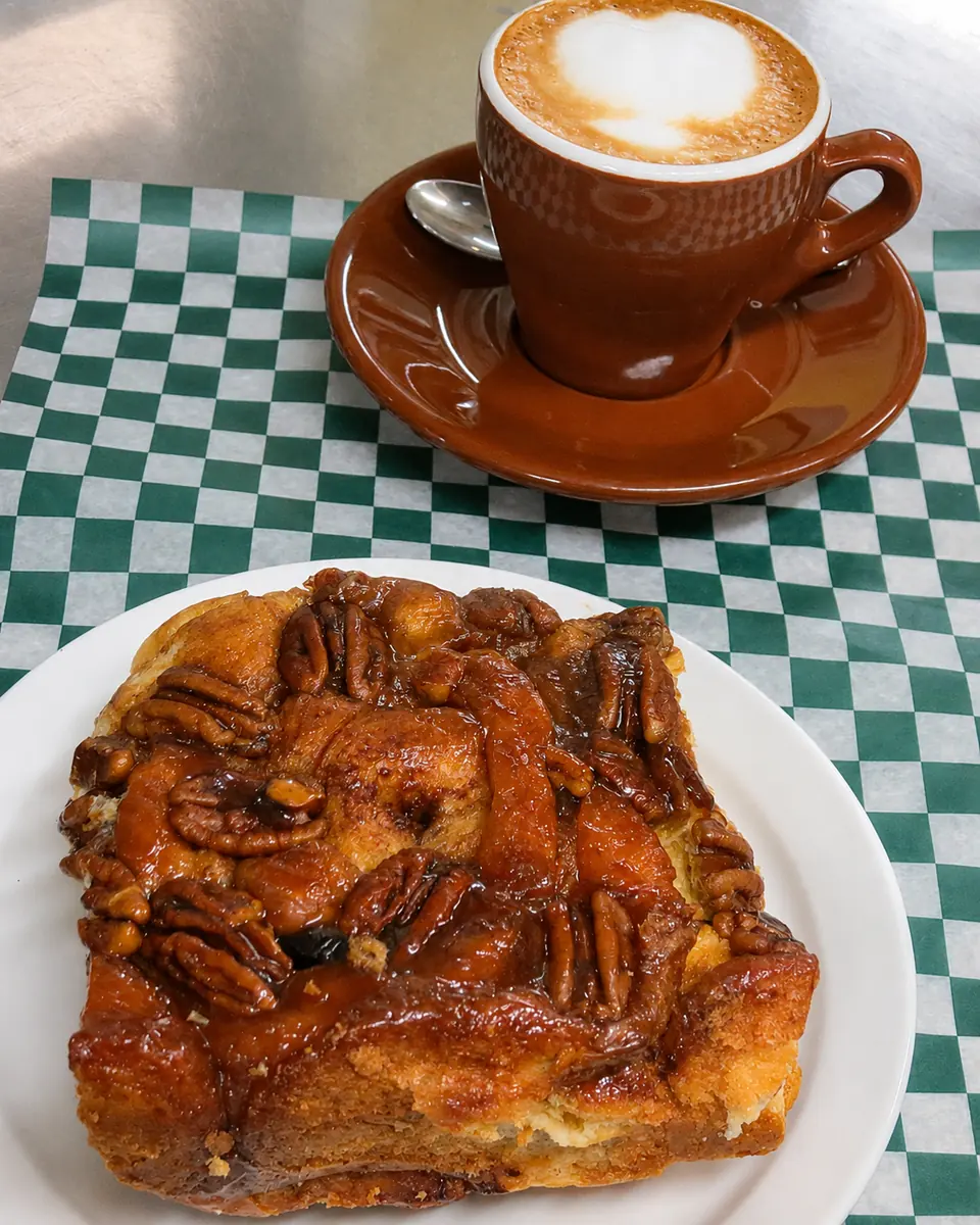 A cup of coffee with a pecan-topped pastry